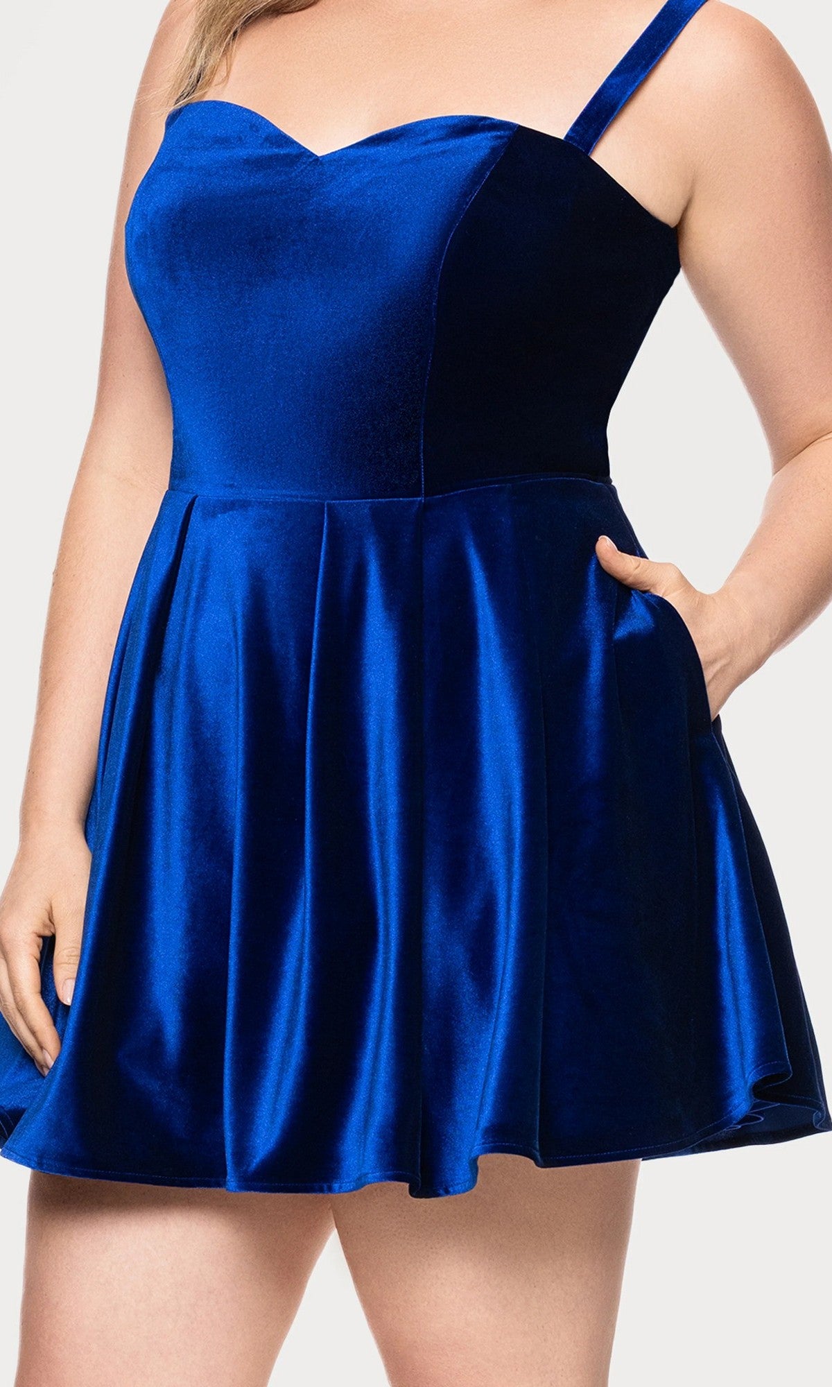 Model wearing the Blondie Nites 4469BNW short plus-size prom dress, featuring a sleeveless royal blue velvet design with a fitted bodice, flared skirt, and side pocket; shown from shoulders to mid-thigh.